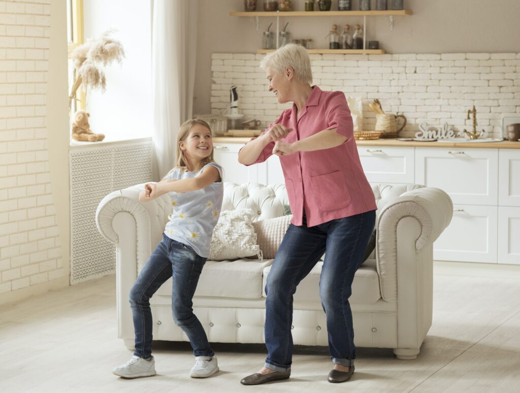 Cheerful older lady with her granddaughter dancing at home